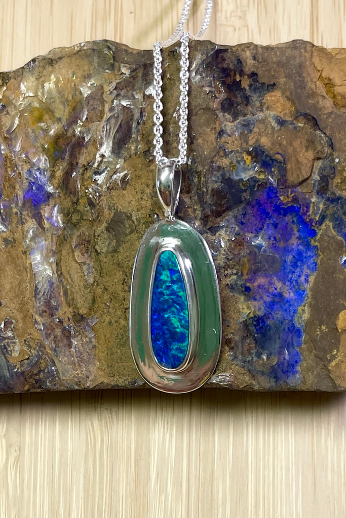 Australian opal pendant is shaped into an abstract shape with a polished frame surrounding it. The flashes of colour in the opal give one a glimpse into the past. 