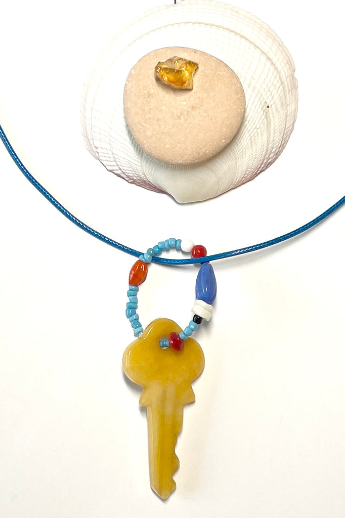 A key made of stone which hangs from a circlet of simple bright village beads. Then suspended from a blue cotton necklace.