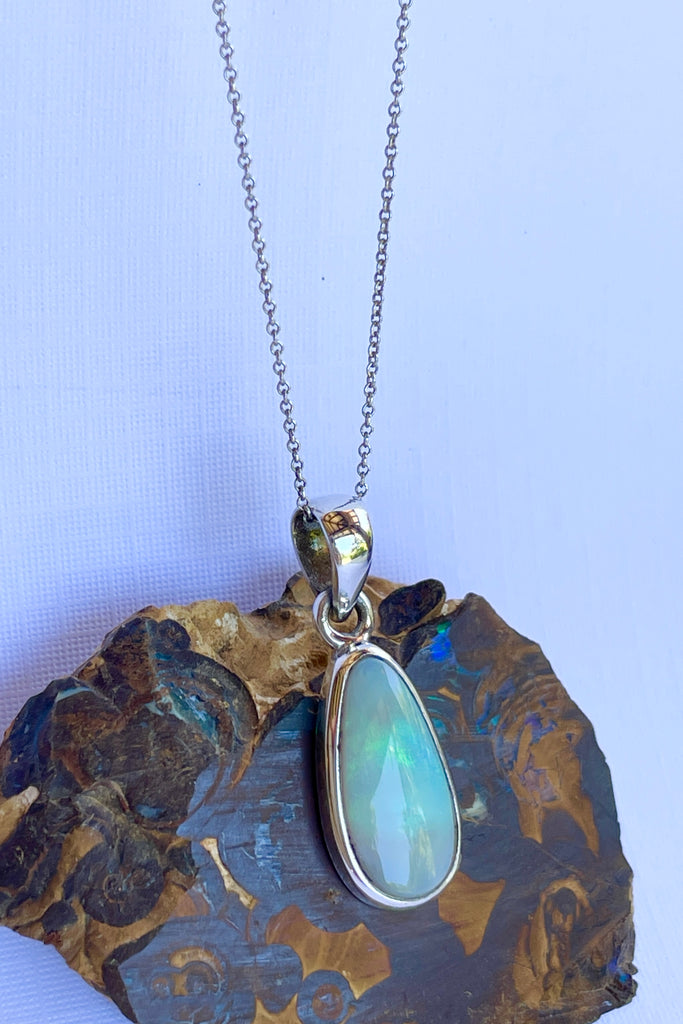 This Australian crystal opal pendant is shaped into an abstract shape with a polished frame surrounding it. The flashes of colour give one a glimpse into the past. 