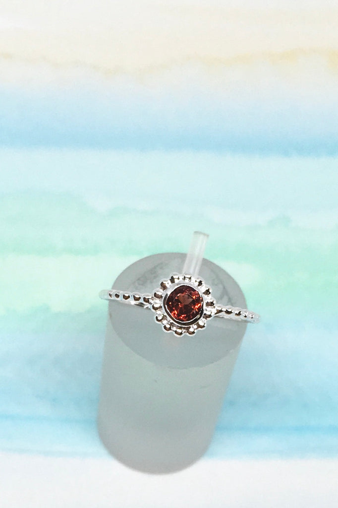  little ring with a faceted garnet gemstone set into a delicate band made up of silver dots.