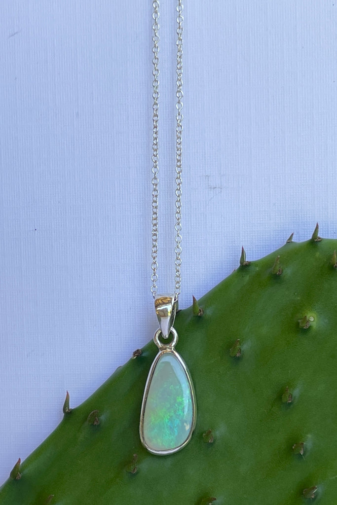This Australian crystal opal pendant is shaped into an abstract shape with a polished frame surrounding it. The flashes of colour give one a glimpse into the past. 