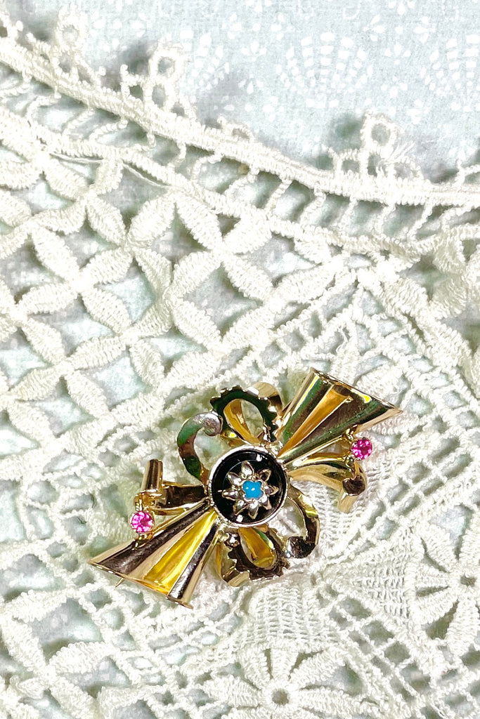 the brooch is unmarked gold with two tiny pink stones either pink garnet or ruby, the centre is black onyx with a star that has a turquoise centre stone.