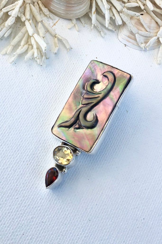 The Echo Pendant Keeper in 925 silver is a substantial piece, there is an exotic foliate design hand carved onto black lip Mother of Pearl. At the base is an oval citrine and a tear drop garnet. 