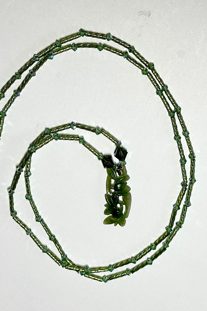 necklace is opera length and can be worn long or doubled to be shorter. Crystal glass bugle beads and green Swarovski crystals. The centre is a pendant of beautifully carved foliage in greenstone jade.