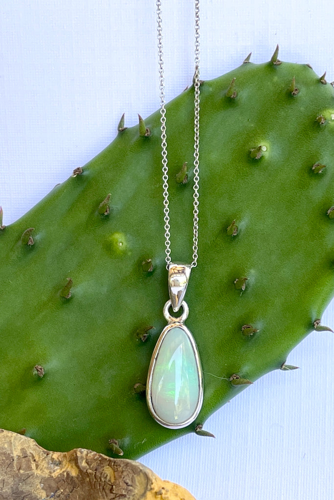 This Australian crystal opal pendant is shaped into an abstract shape with a polished frame surrounding it. The flashes of colour give one a glimpse into the past. 