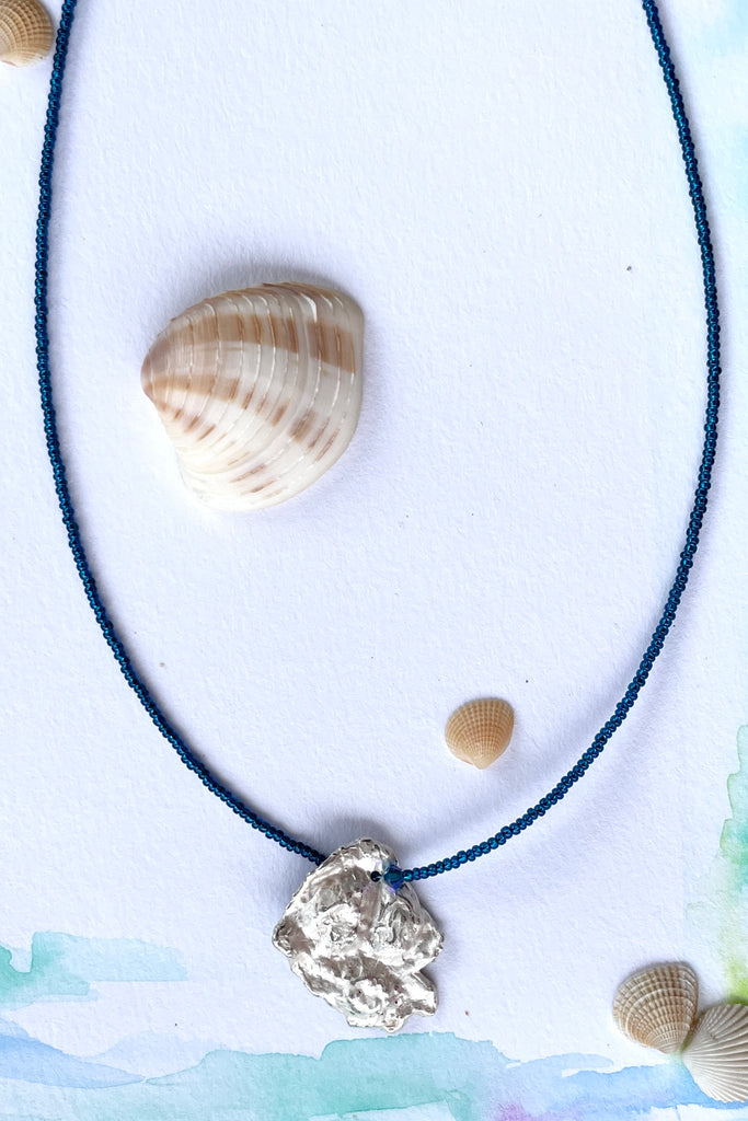 The centre piece is silver, it is cast from a shard of shell picked up on the Noosa beach. This organic shape of this pendant  is very unusual and unique. The underside is enameled in the colours of sea blue, with a scattering of sand and rocks, and bubbles. 