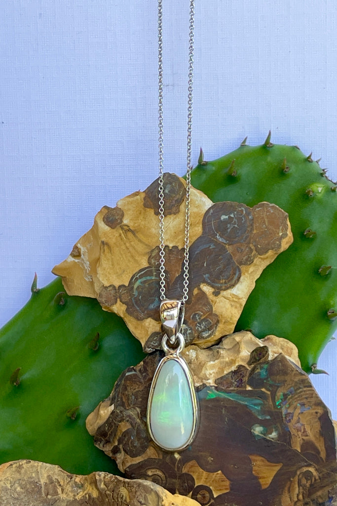 This Australian crystal opal pendant is shaped into an abstract shape with a polished frame surrounding it. The flashes of colour give one a glimpse into the past. 