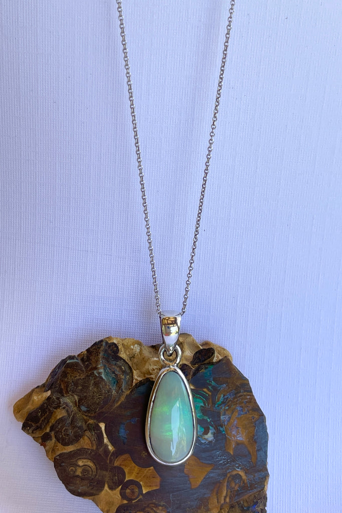 This Australian crystal opal pendant is shaped into an abstract shape with a polished frame surrounding it. The flashes of colour give one a glimpse into the past. 