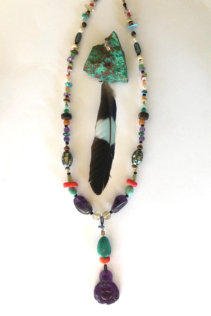 The elegant centre piece of this divine necklace is a mystical Deity carved in clear purple Amethyst and other stones on the chain include Peridot, Bad Howlite, Paua shell mosaic bead, green onyx, Carnelian, Amethyst, Golden Rutile Crystal and wood.