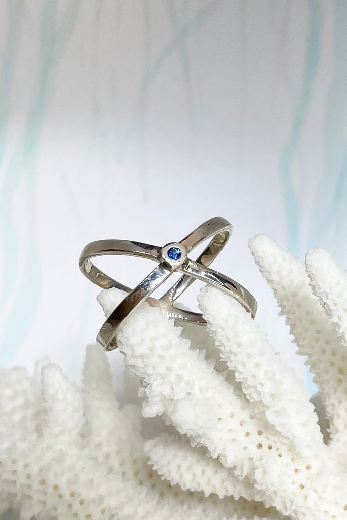 A simple Modern ring in minimal design in 925 silver. Features a small natural blue sapphire in the centre of two overlapping silver orbits.