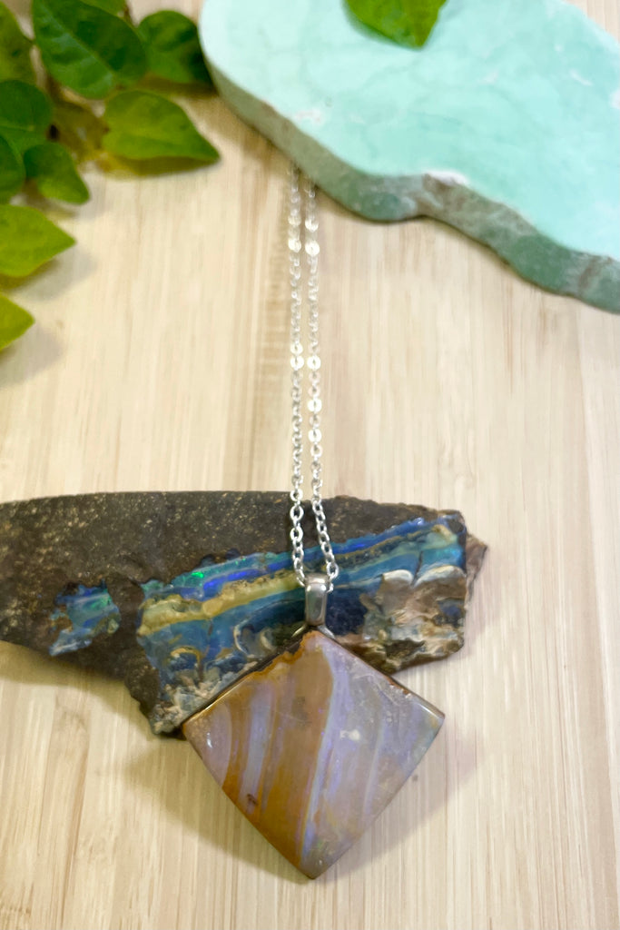This opal is cut into a rough long triangle shape it has pale pinky blue opal flash with tiny flashes of green on the side. The face still shows some of the host rock from which it was cut.