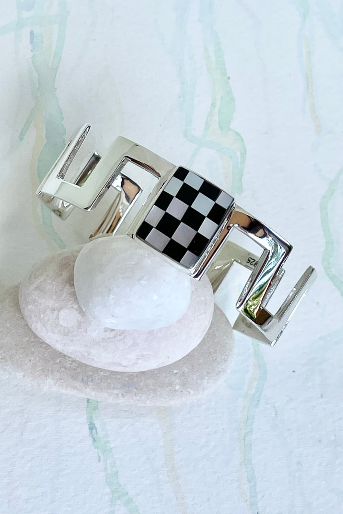 Very cool and sophisticated, this 925 silver cuff bracelet rocks the modern retro cool. In a square geometric design featuring a centre square inlaid with mother of pearl and black enamel,