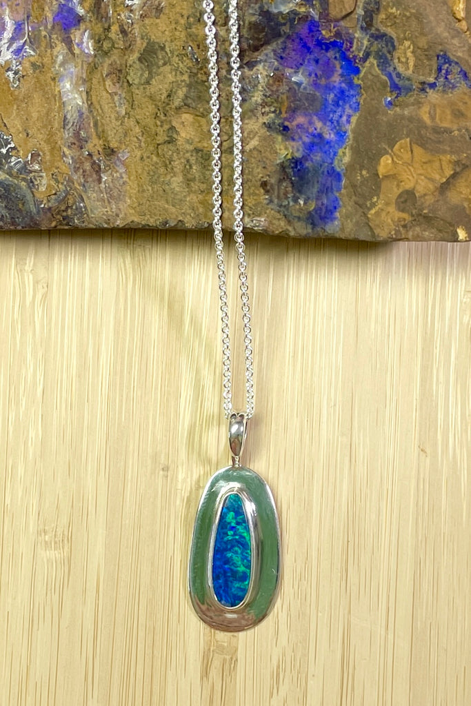 Australian opal pendant is shaped into an abstract shape with a polished frame surrounding it. The flashes of colour in the opal give one a glimpse into the past. 