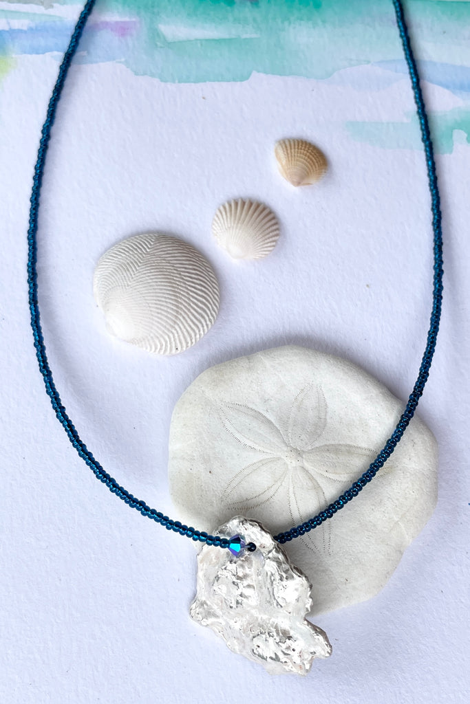 The centre piece is silver, it is cast from a shard of shell picked up on the Noosa beach. This organic shape of this pendant  is very unusual and unique. The underside is enameled in the colours of sea blue, with a scattering of sand and rocks, and bubbles. 