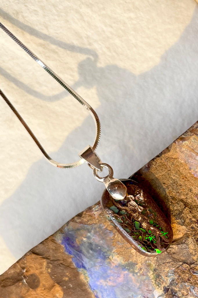 This opal has a lovely green flash across the centre of the stone, it is cut into a rounded oval and shows the mark of the artist who cut and polished the stone. It has a river of blue running down one side. This genuine Australian Boulder Opal stone was cut and polished in Queensland by an Opal miner.