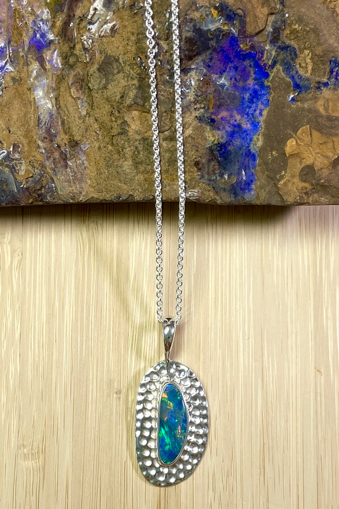 Australian opal pendant is shaped into an abstract shape with a polished frame surrounding it. The flashes of colour in the opal give one a glimpse into the past. 