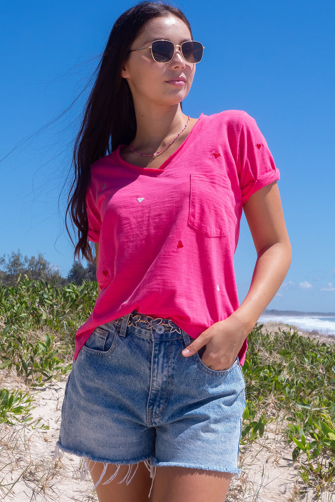 The Aurora T-Shirt Love Heart Red is a hot pink, relaxed fit, t-shirt with embroidered red and white hearts all over. The shirt features a raw edged v-neck, front breast pocket, side spilt and rolled sleeve. Made from Knit 95% cotton / 5% spandex.