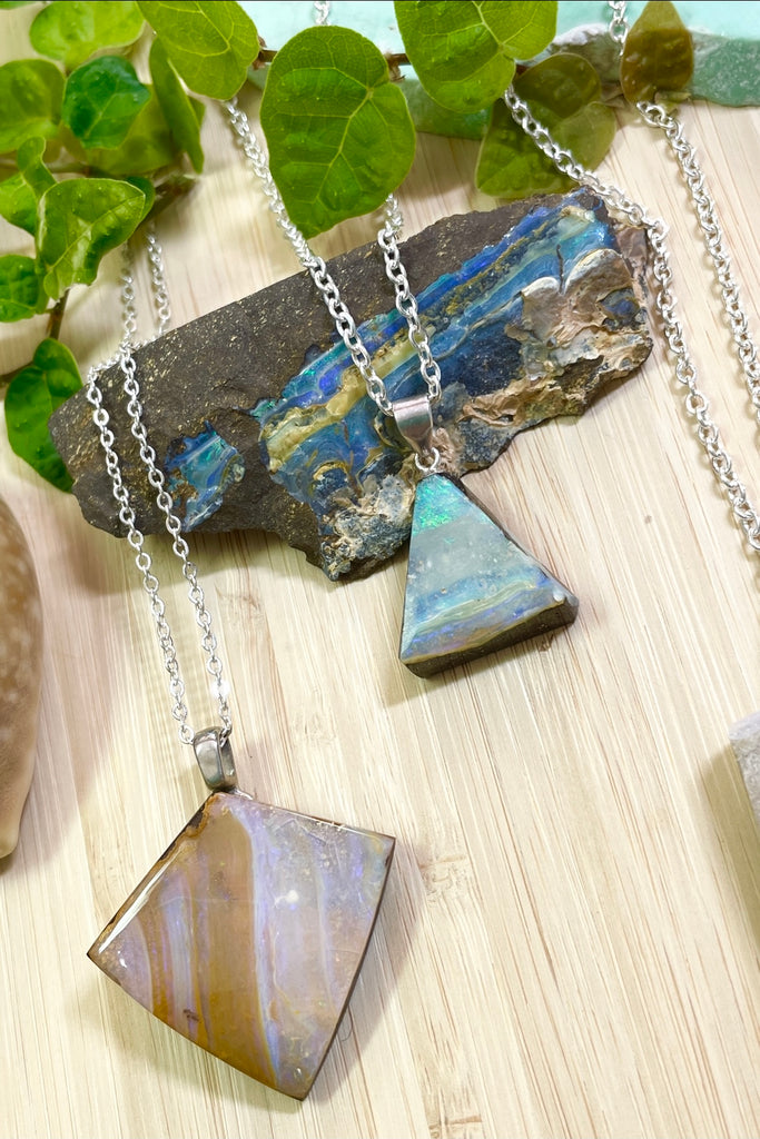 This opal is cut into a rough long triangle shape it has pale pinky blue opal flash with tiny flashes of green on the side. The face still shows some of the host rock from which it was cut.