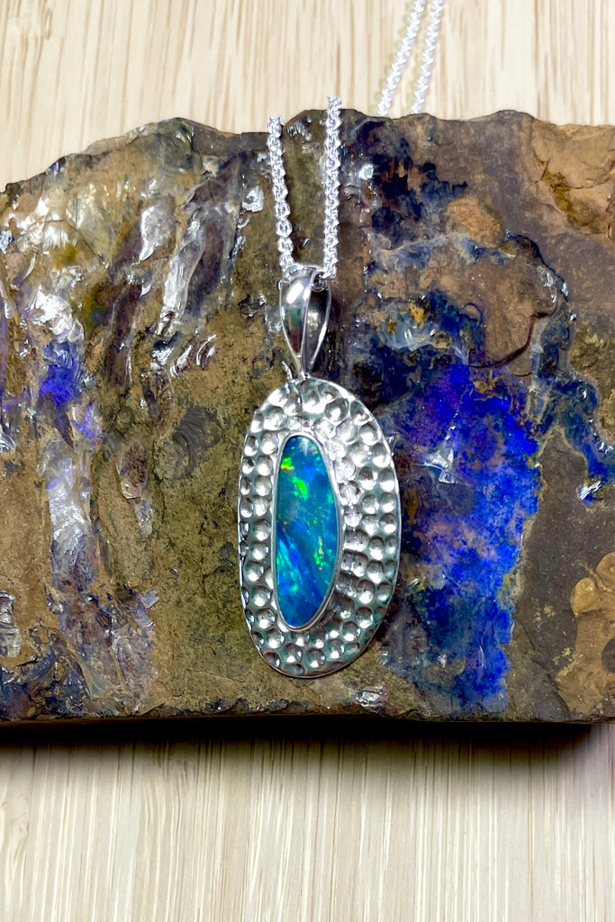 Australian opal pendant is shaped into an abstract shape with a polished frame surrounding it. The flashes of colour in the opal give one a glimpse into the past. 