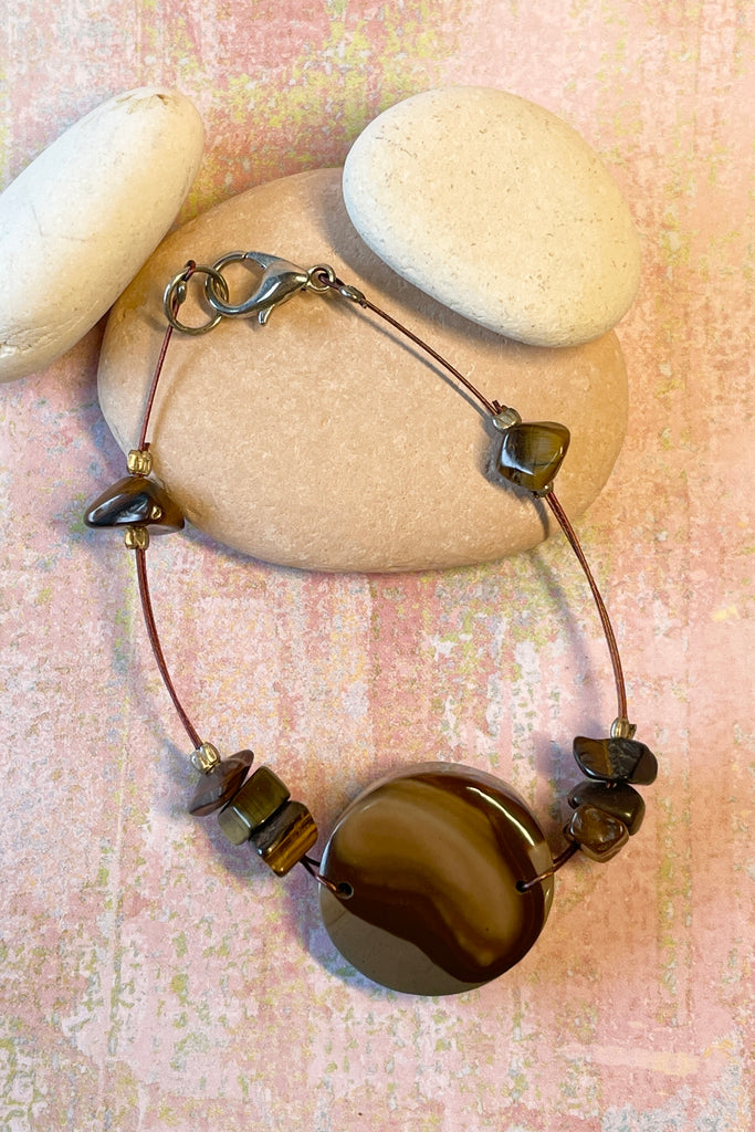 A handmade bangle with a centre piece of Agate stone which has been cut and polished by ROAM Ladies Lapidary Collective in Sakaraha, Madagascar. The band isTigers Eye chip beads. This collective was created with aid funds from the Australia