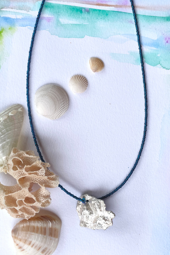 The centre piece is silver, it is cast from a shard of shell picked up on the Noosa beach. This organic shape of this pendant  is very unusual and unique. The underside is enameled in the colours of sea blue, with a scattering of sand and rocks, and bubbles. 