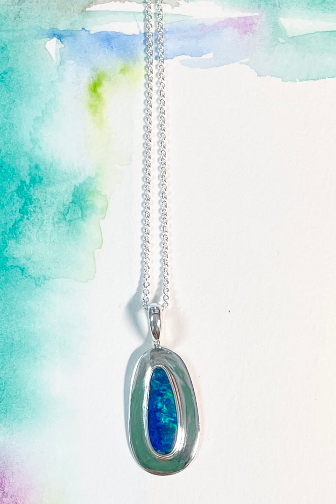 Australian opal pendant is shaped into an abstract shape with a polished frame surrounding it. The flashes of colour in the opal give one a glimpse into the past. 