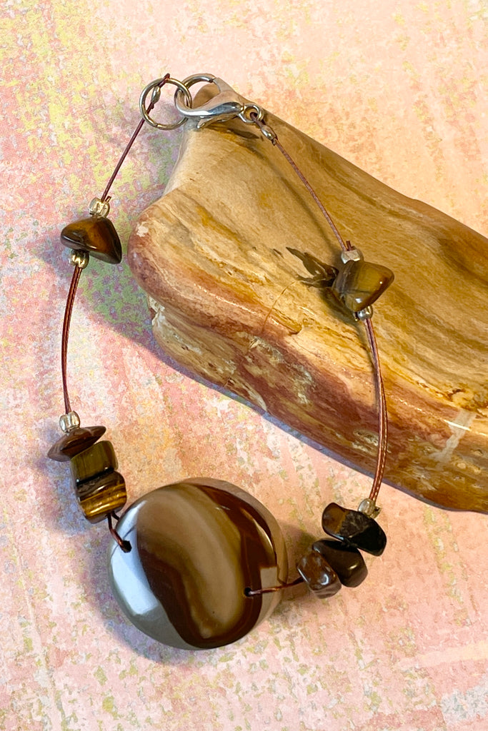 A handmade bangle with a centre piece of Agate stone which has been cut and polished by ROAM Ladies Lapidary Collective in Sakaraha, Madagascar. The band isTigers Eye chip beads. This collective was created with aid funds from the Australia