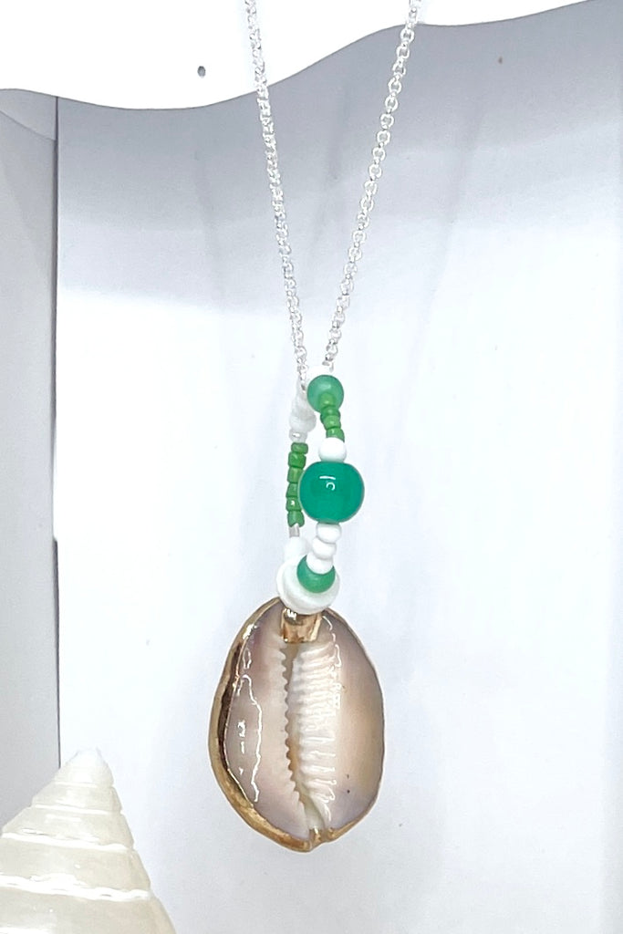 A pendant keepsake made with a cowrie shell which hangs from a circlet of simple green and white village beads. Then suspended from a chain.