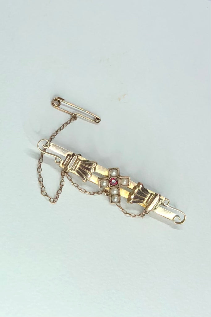  In 9ct gold it has a classical semi foliate on each side of a cross which is decorated with a single ruby and five half pearls, 