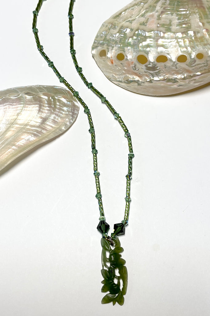 necklace is opera length and can be worn long or doubled to be shorter. Crystal glass bugle beads and green Swarovski crystals. The centre is a pendant of beautifully carved foliage in greenstone jade.
