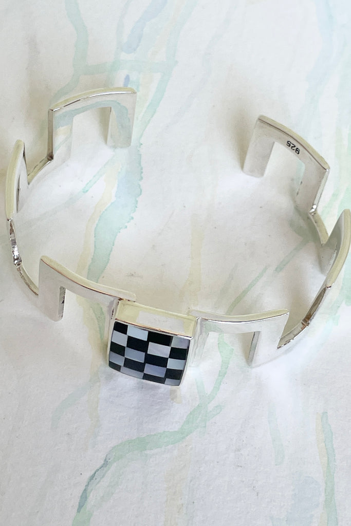 Very cool and sophisticated, this 925 silver cuff bracelet rocks the modern retro cool. In a square geometric design featuring a centre square inlaid with mother of pearl and black enamel,