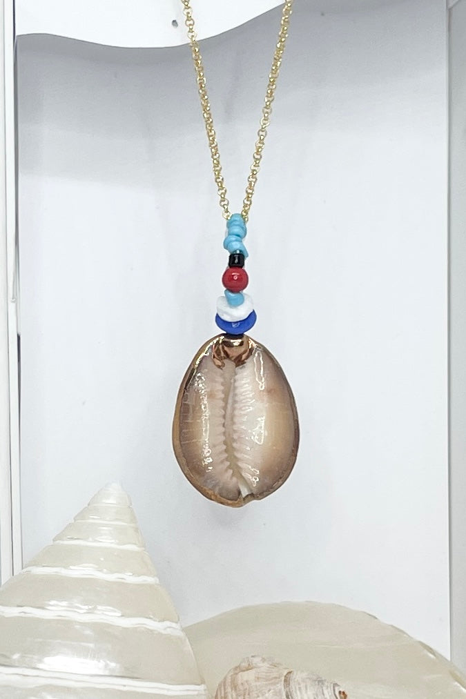 A pendant keepsake made with a cowrie shell which hangs from a circlet of simple green and white village beads. Then suspended from a chain.