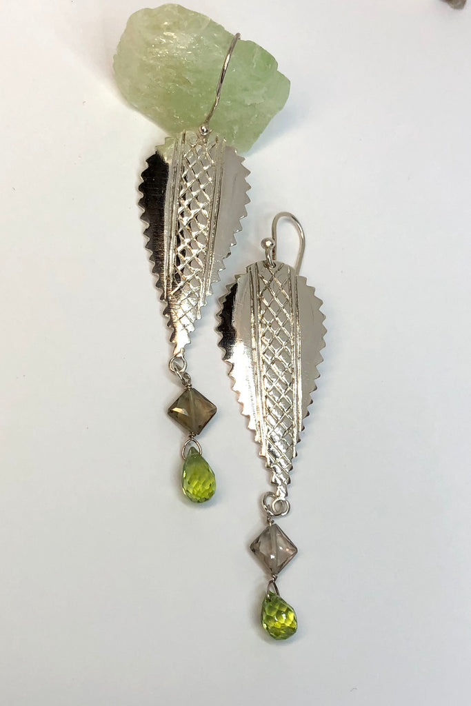 The African inspired design of these earrings was obtained by casting a pair of Mozambique Ebony wood earrings in silver. A Peridot gemstone briolet and a faceted smoky quartz hang from the base. 