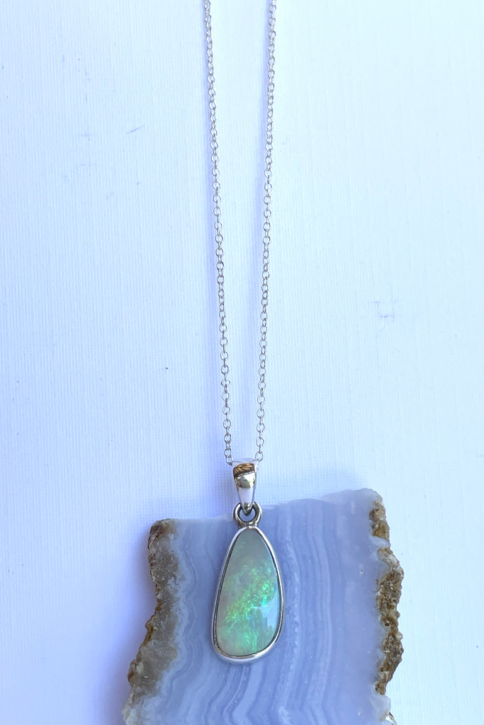 This Australian crystal opal pendant is shaped into an abstract shape with a polished frame surrounding it. The flashes of colour give one a glimpse into the past. 