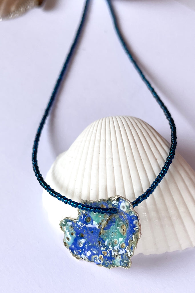 The centre piece is silver, it is cast from a shard of shell picked up on the Noosa beach. This organic shape of this pendant  is very unusual and unique. The underside is enameled in the colours of sea blue, with a scattering of sand and rocks, and bubbles. 