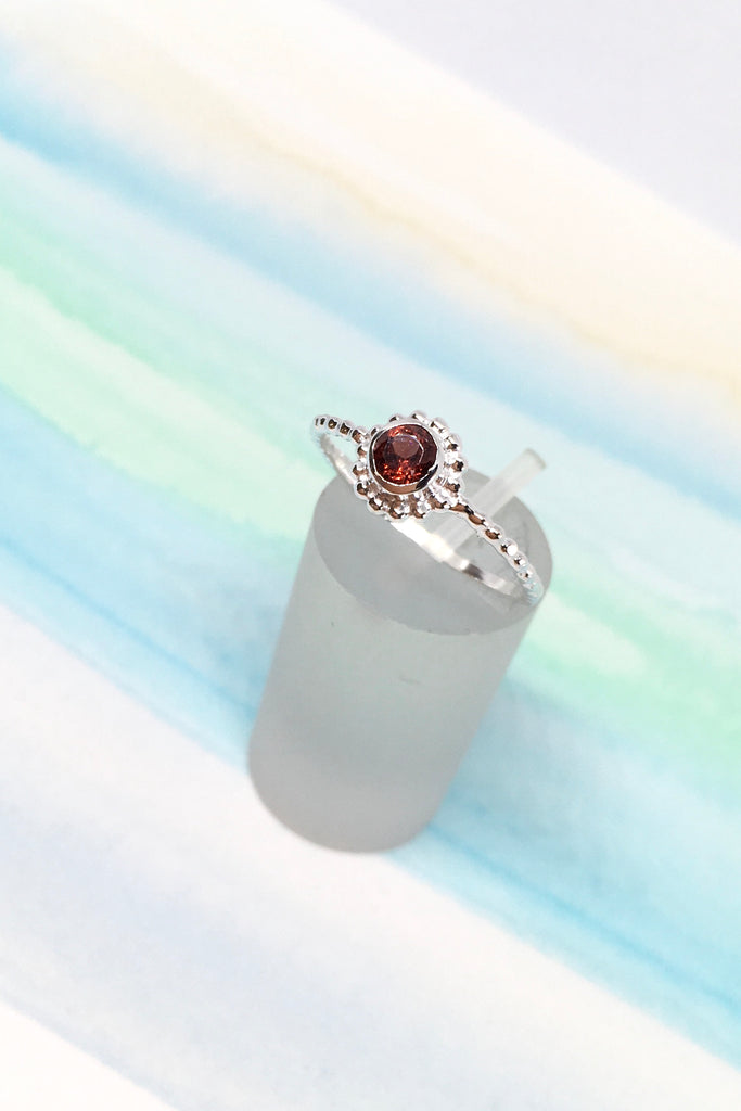  little ring with a faceted garnet gemstone set into a delicate band made up of silver dots.
