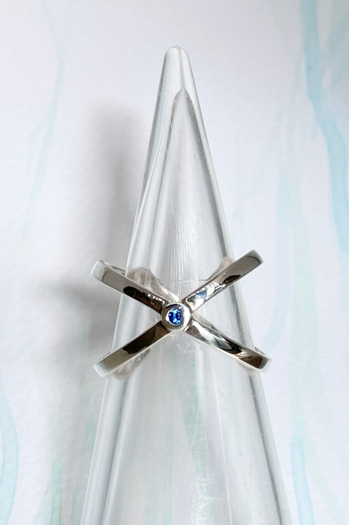 A simple Modern ring in minimal design in 925 silver. Features a small natural blue sapphire in the centre of two overlapping silver orbits.
