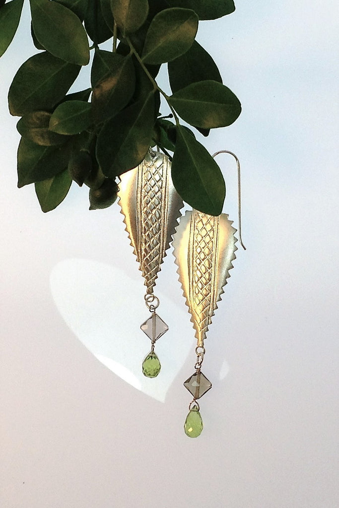 The African inspired design of these earrings was obtained by casting a pair of Mozambique Ebony wood earrings in silver. A Peridot gemstone briolet and a faceted smoky quartz hang from the base. 