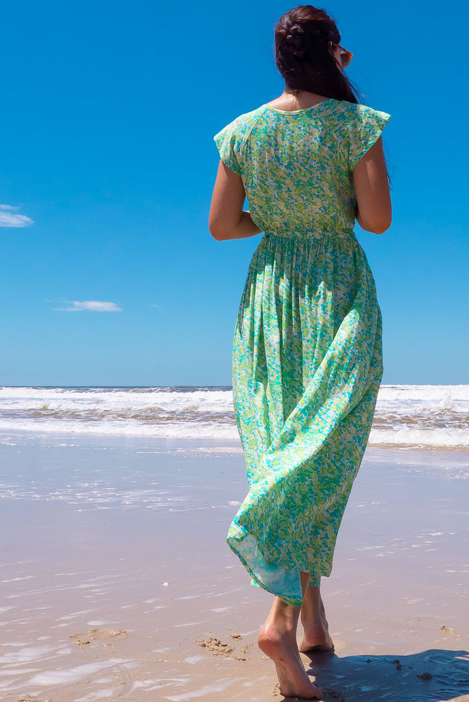 The Juniper Green Lemonade Maxi Dress is a vibrant green floral printed dress. The maxi dress features a functional button down chest to waistline, side pockets, adjustable drawstring waist, and cap sleeves. Made form woven 100% rayon.