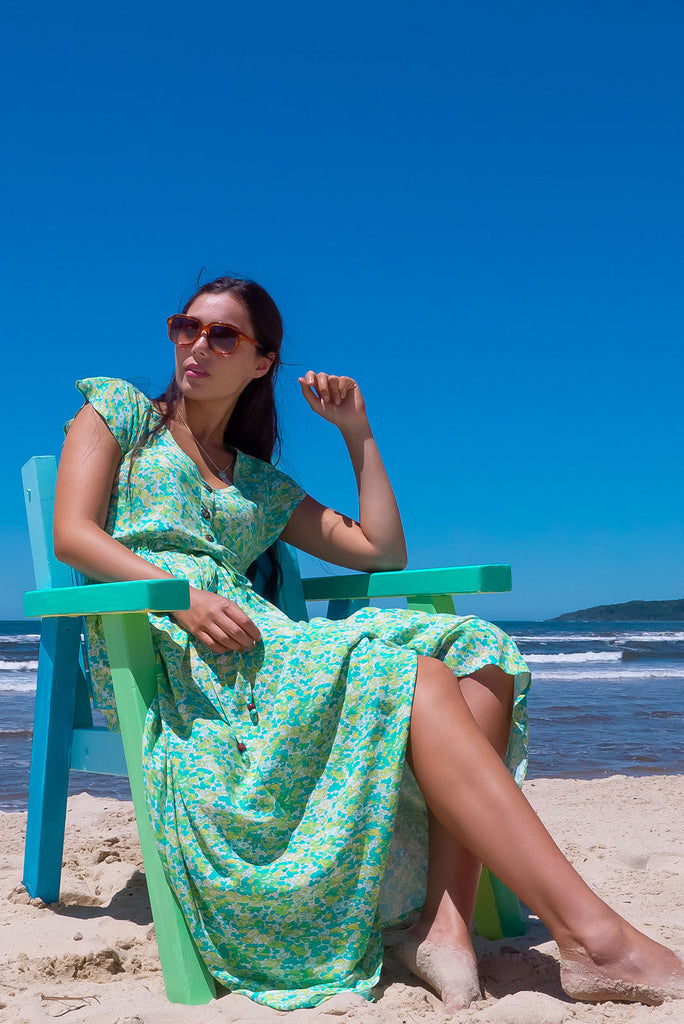 The Juniper Green Lemonade Maxi Dress is a vibrant green floral printed dress. The maxi dress features a functional button down chest to waistline, side pockets, adjustable drawstring waist, and cap sleeves. Made form woven 100% rayon.