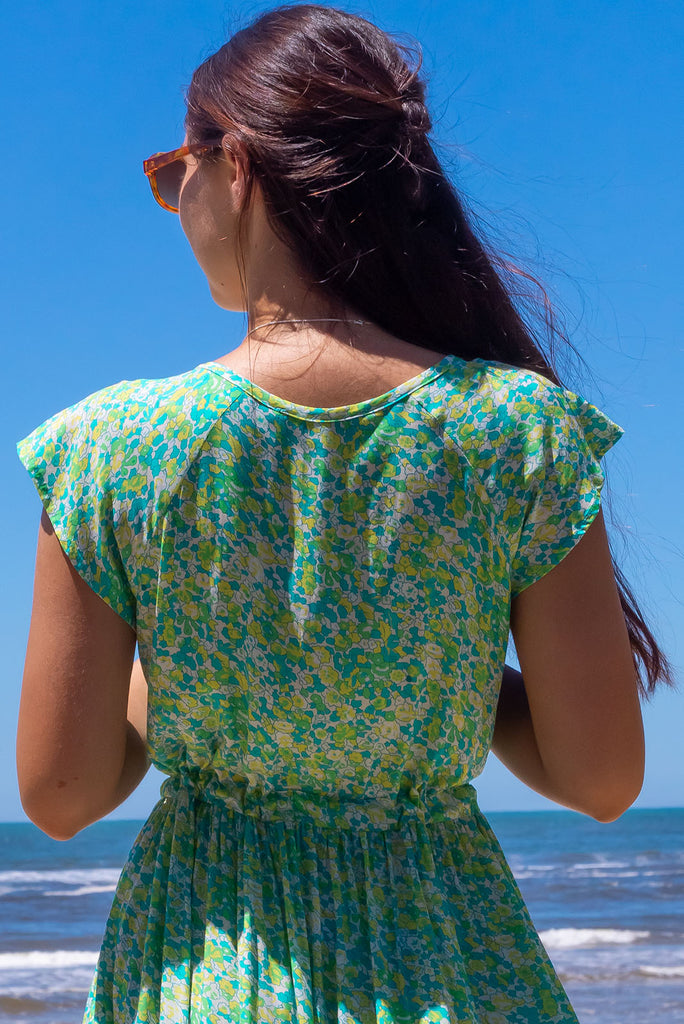 The Juniper Green Lemonade Maxi Dress is a vibrant green floral printed dress. The maxi dress features a functional button down chest to waistline, side pockets, adjustable drawstring waist, and cap sleeves. Made form woven 100% rayon.