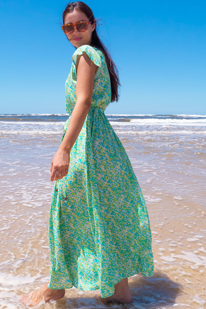 The Juniper Green Lemonade Maxi Dress is a vibrant green floral printed dress. The maxi dress features a functional button down chest to waistline, side pockets, adjustable drawstring waist, and cap sleeves. Made form woven 100% rayon.
