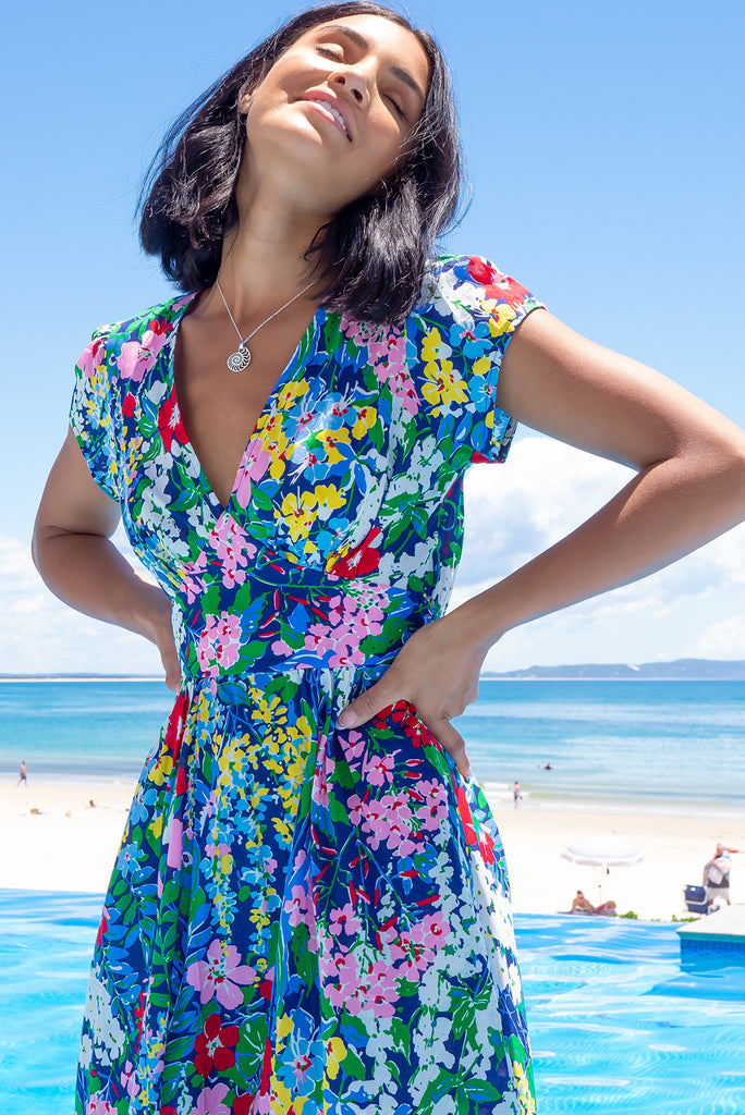 This Style Features A Deep V Neckline, Fitted Basque Waist With Gathered Bust, Side Pockets, Cap Sleeves And Elasticated Back For Maximum Comfort. The Monet Print Is A Navy Base Adorned With Pin, Red, Yellow, Blue, Green And White Medium Sized Florals. Made From 100% Cotton