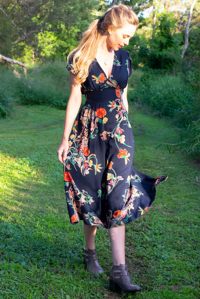 Lizzie Navy Bouquet Midi Dress features fitted elasticated waist, a cap sleeve and deep v neck and it comes in a dark navy with multicoloured floral design on a soft woven 100% rayon, perfect for vintage style lover.