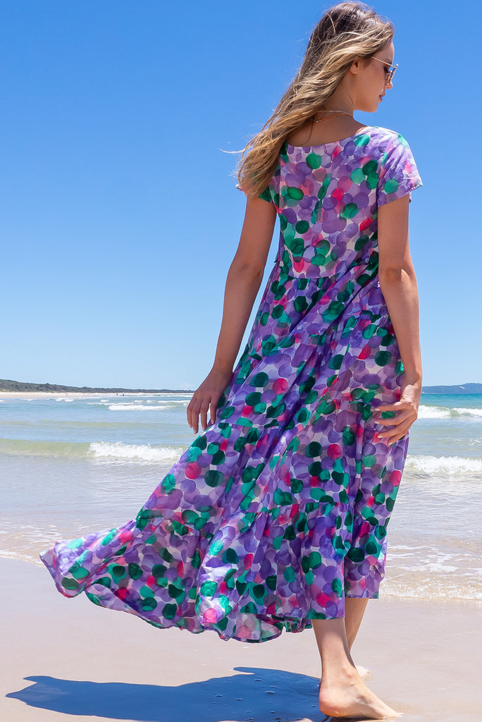 Our Lucky Lulu Is A Maxi Length Dress Featuring A Scooped Neckline, Adjustable Waist Tabs, Side Pockets And A Wide Tiered Skirt. The Bubbles Print Is A White Base With Purple, Green And Pink Wash Effect Bubbles All Over. Made From 100% Cotton.
