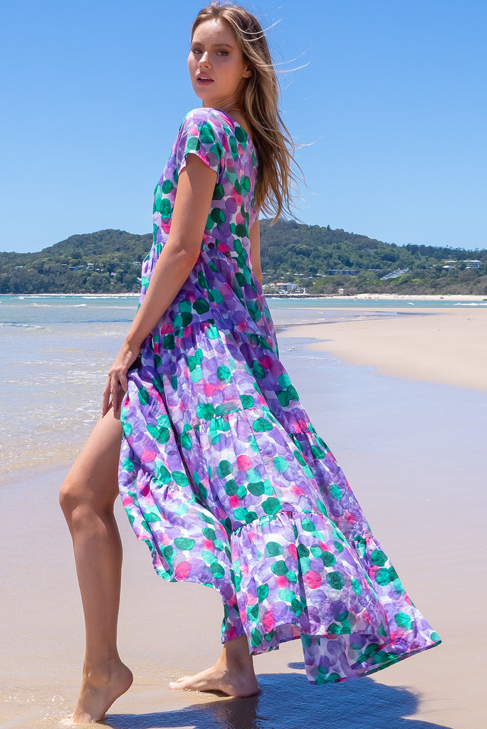 Our Lucky Lulu Is A Maxi Length Dress Featuring A Scooped Neckline, Adjustable Waist Tabs, Side Pockets And A Wide Tiered Skirt. The Bubbles Print Is A White Base With Purple, Green And Pink Wash Effect Bubbles All Over. Made From 100% Cotton.