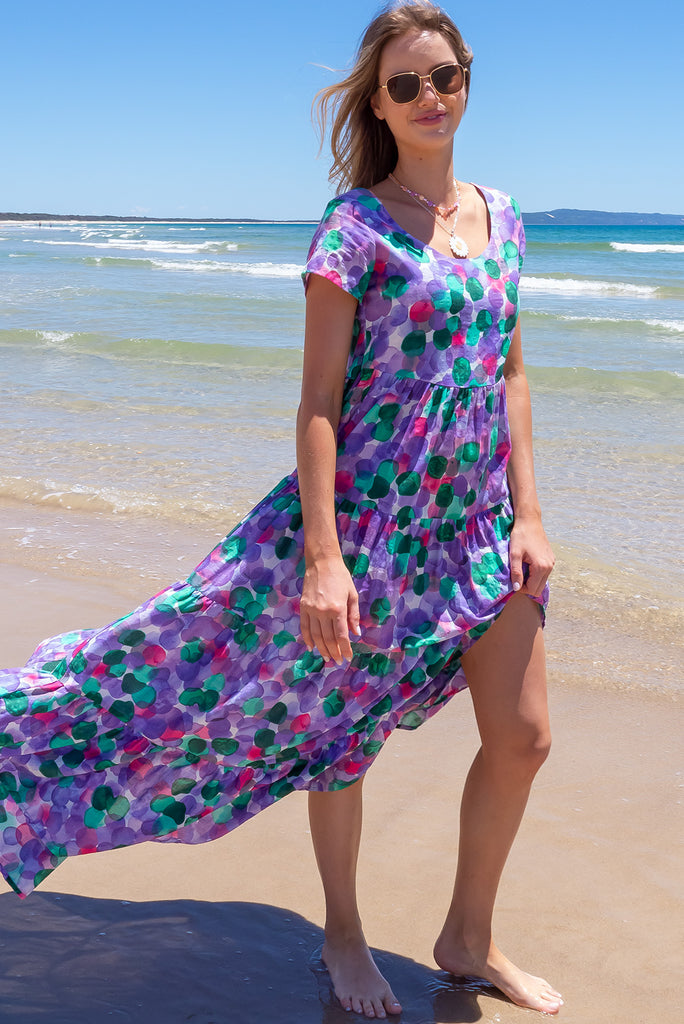 Our Lucky Lulu Is A Maxi Length Dress Featuring A Scooped Neckline, Adjustable Waist Tabs, Side Pockets And A Wide Tiered Skirt. The Bubbles Print Is A White Base With Purple, Green And Pink Wash Effect Bubbles All Over. Made From 100% Cotton.