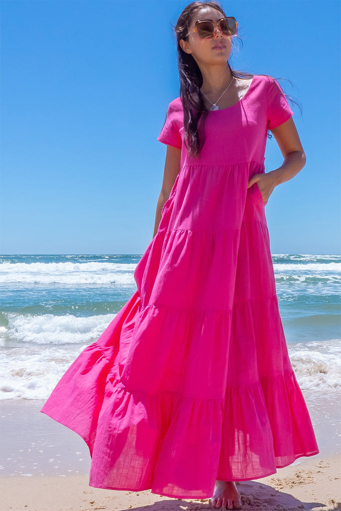 The Lucky Lulu Candy Tiered Maxi Dress is a stunning hot pink maxi dress. This dress features a scooped neckline, adjustable waist tabs, side pockets and a wide tiered skirt. Made from woven 100% cotton.