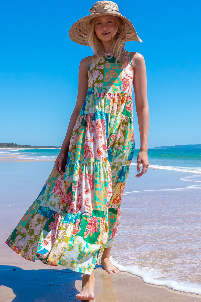 The Lulu Darling Green Glow Maxi Dress features a high neck with thin straps, high cut under arms, full tiered skirting from the bust down and deep side pockets. The dress has a green patchwork print with multicoloured paisley designs. Made from 100% cotton.
