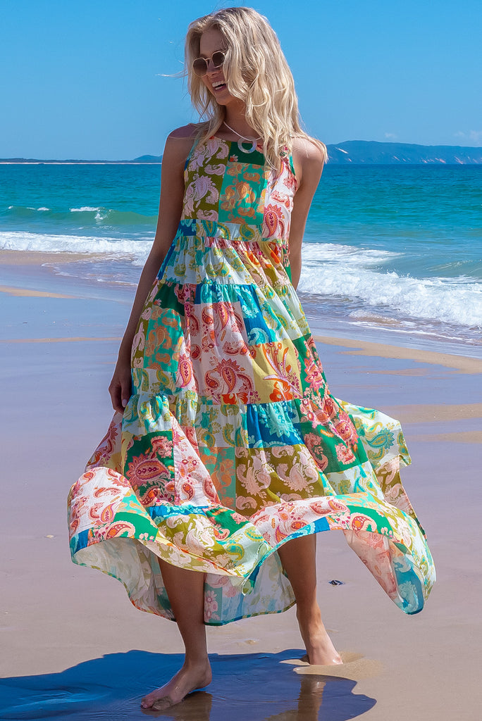 The Lulu Darling Green Glow Maxi Dress features a high neck with thin straps, high cut under arms, full tiered skirting from the bust down and deep side pockets. The dress has a green patchwork print with multicoloured paisley designs. Made from 100% cotton.